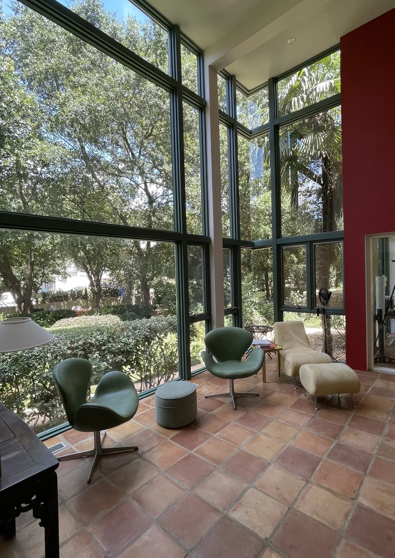 Harmon Residence living space with expansive green-framed windows and terracotta tile floors showcases a high ceiling and natural light.