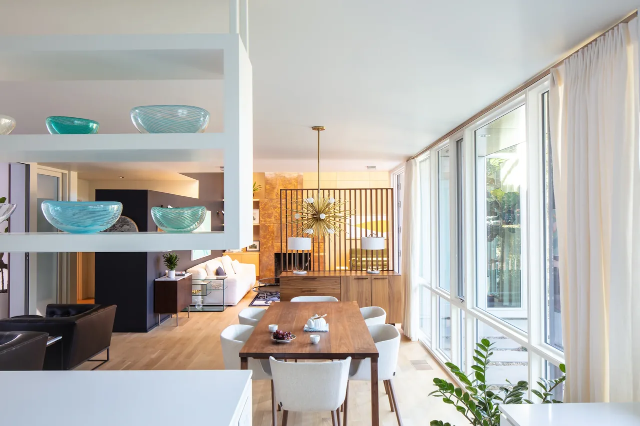 The Sepi Residence dining space features a wooden table with modern white chairs and floor-to-ceiling windows letting in natural light.