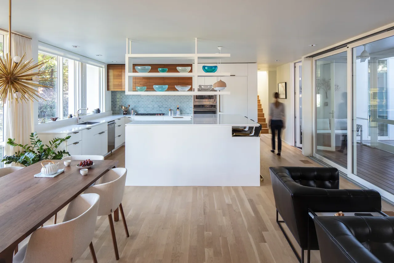 The Sepi Residence kitchen features white cabinetry, wood accents, and a blue tiled backsplash, blending into a dining area with wood table and light chairs.