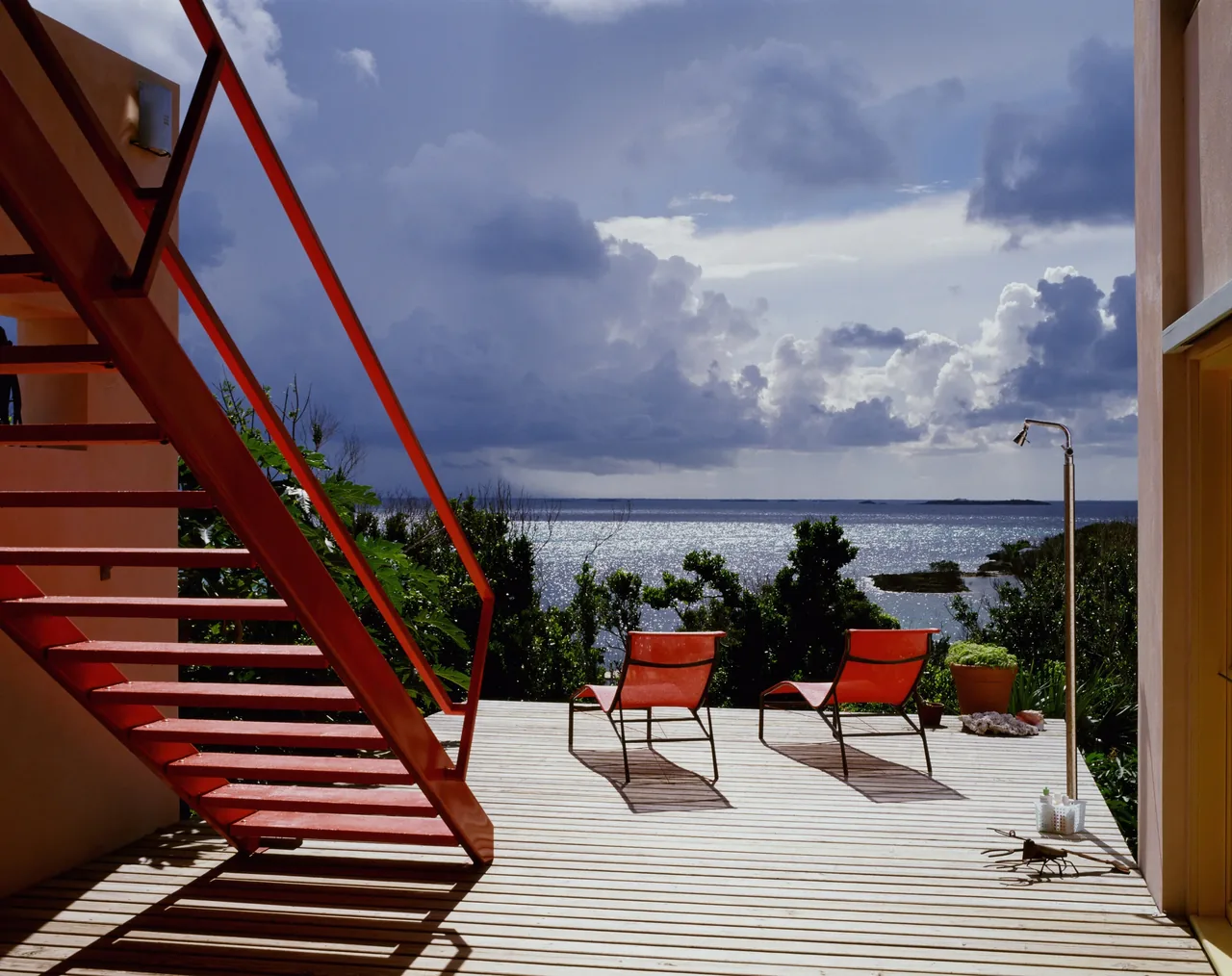 Deck with red metal stairs, red lounge chairs, and an outdoor shower overlooking water at Taylor Vacation Home.