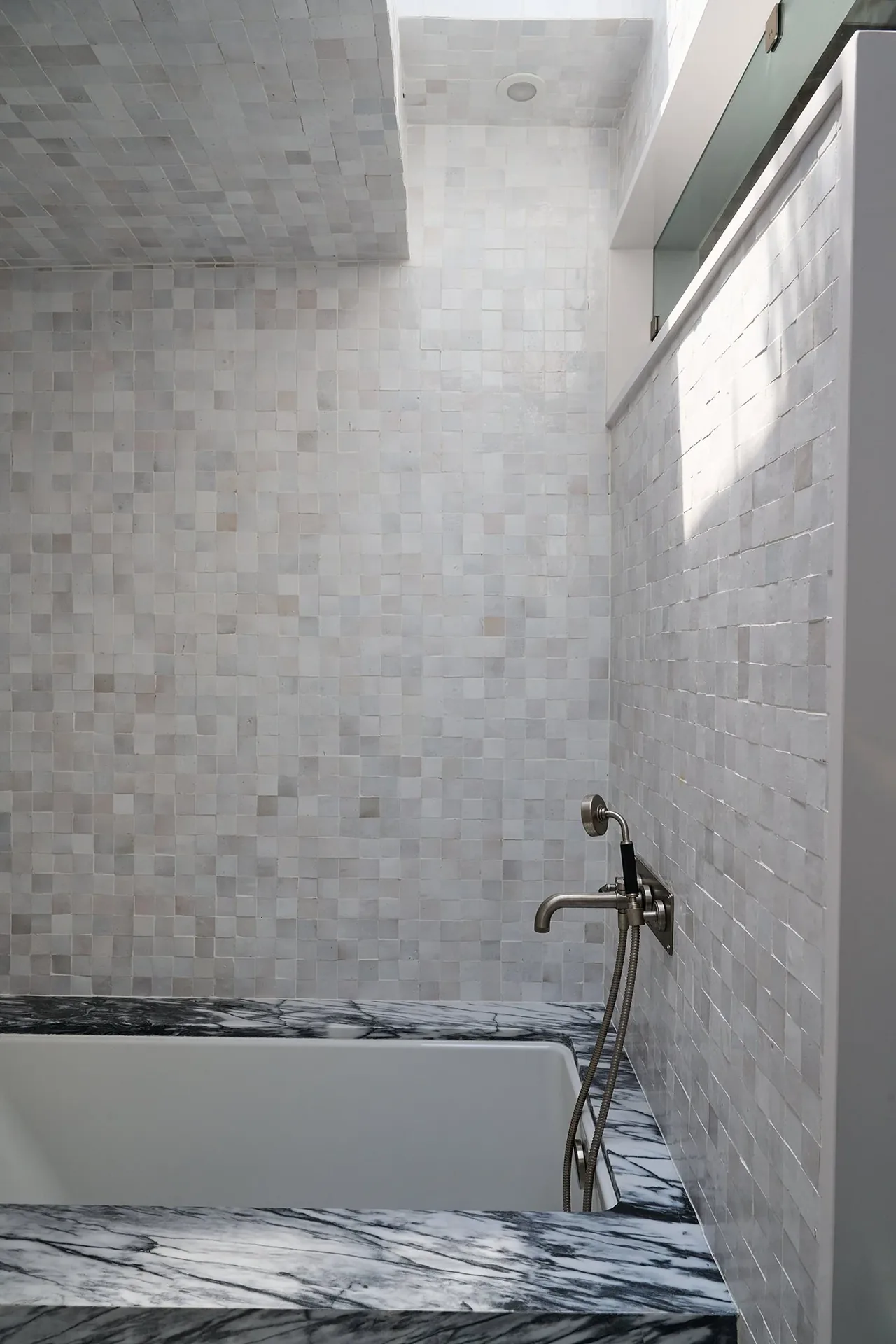 Modern bathroom features white tiled walls and a marble bathtub surround with a wall-mounted faucet.