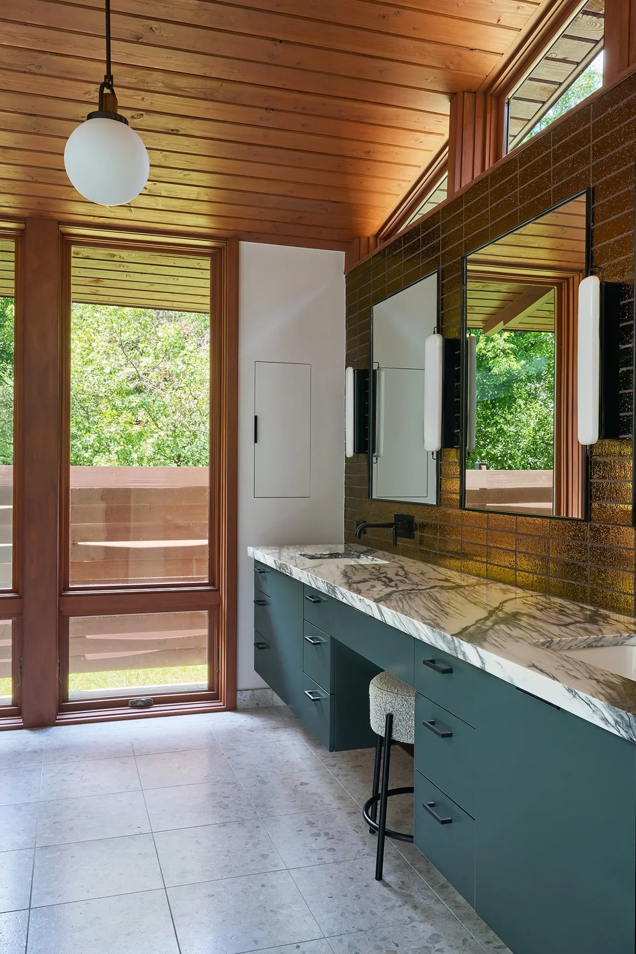 Bathroom with floating vanity, marble countertop, and large wood-framed windows showing greenery outside.
