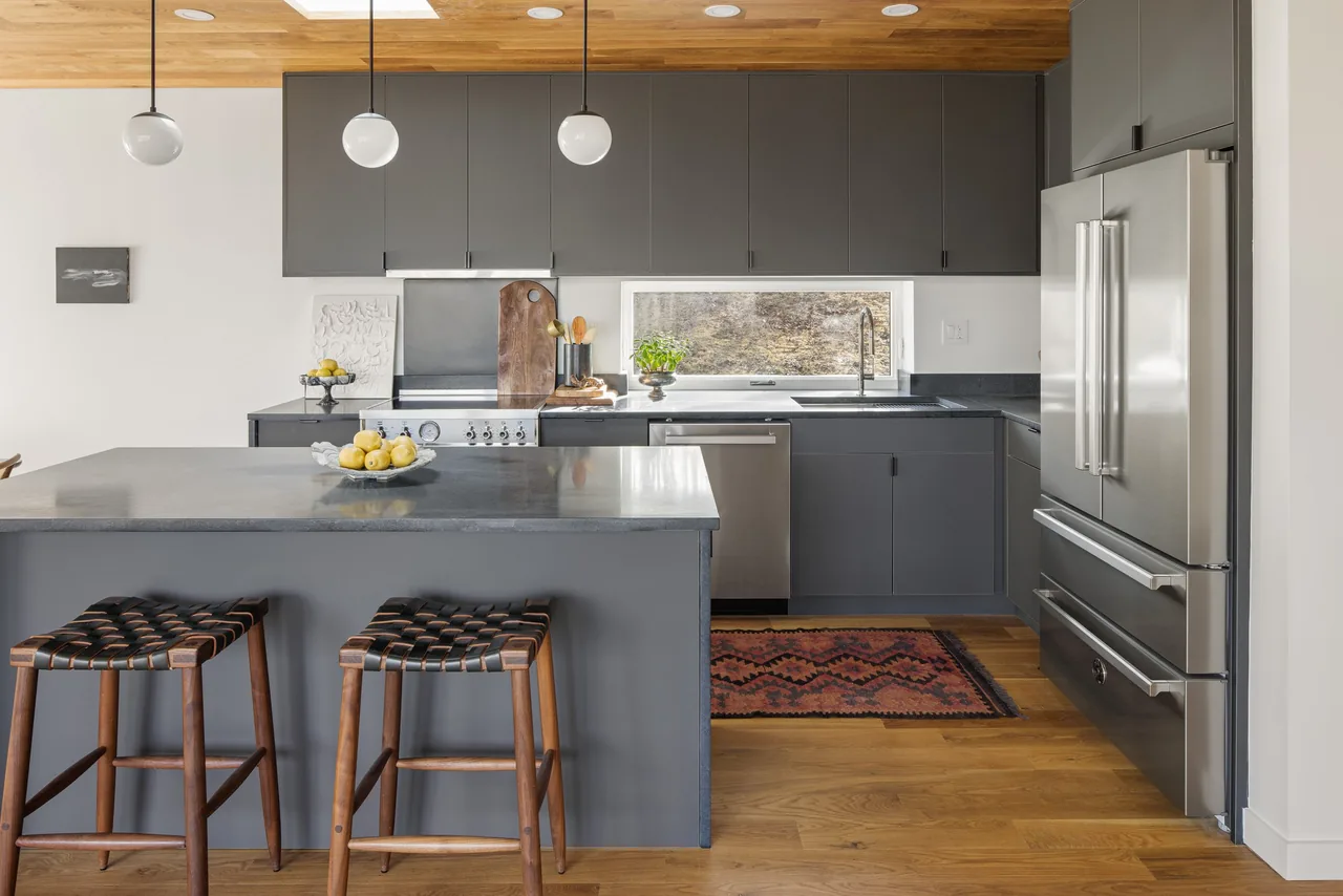 The NZ99 House kitchen features grey cabinetry, a concrete countertop island, and a horizontal window providing natural light.