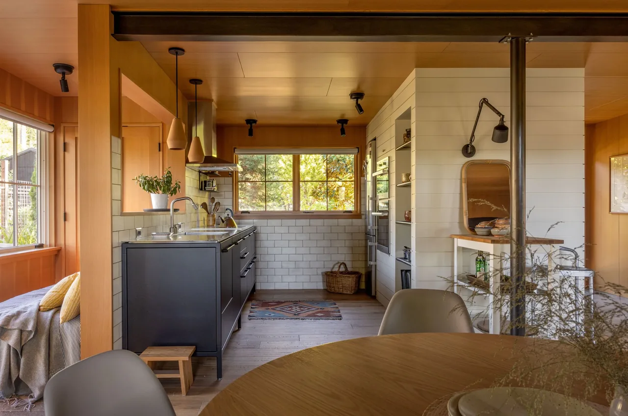 Eagle Harbor Residence kitchen features black lower cabinets, white subway tiles, wood panel walls, and pendant lighting by Graham Baba Architects.