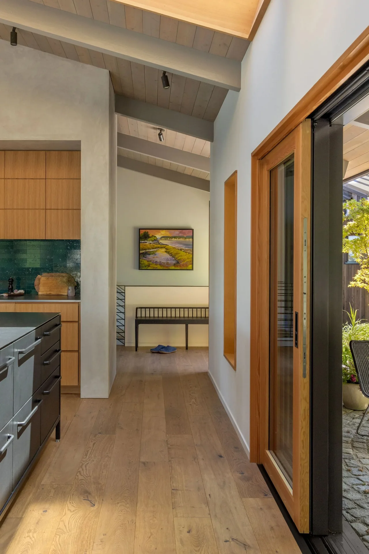 Interior shot of Eagle Harbor Residence hallway beside kitchen with wood ceiling beams and sliding glass door to outdoor space.