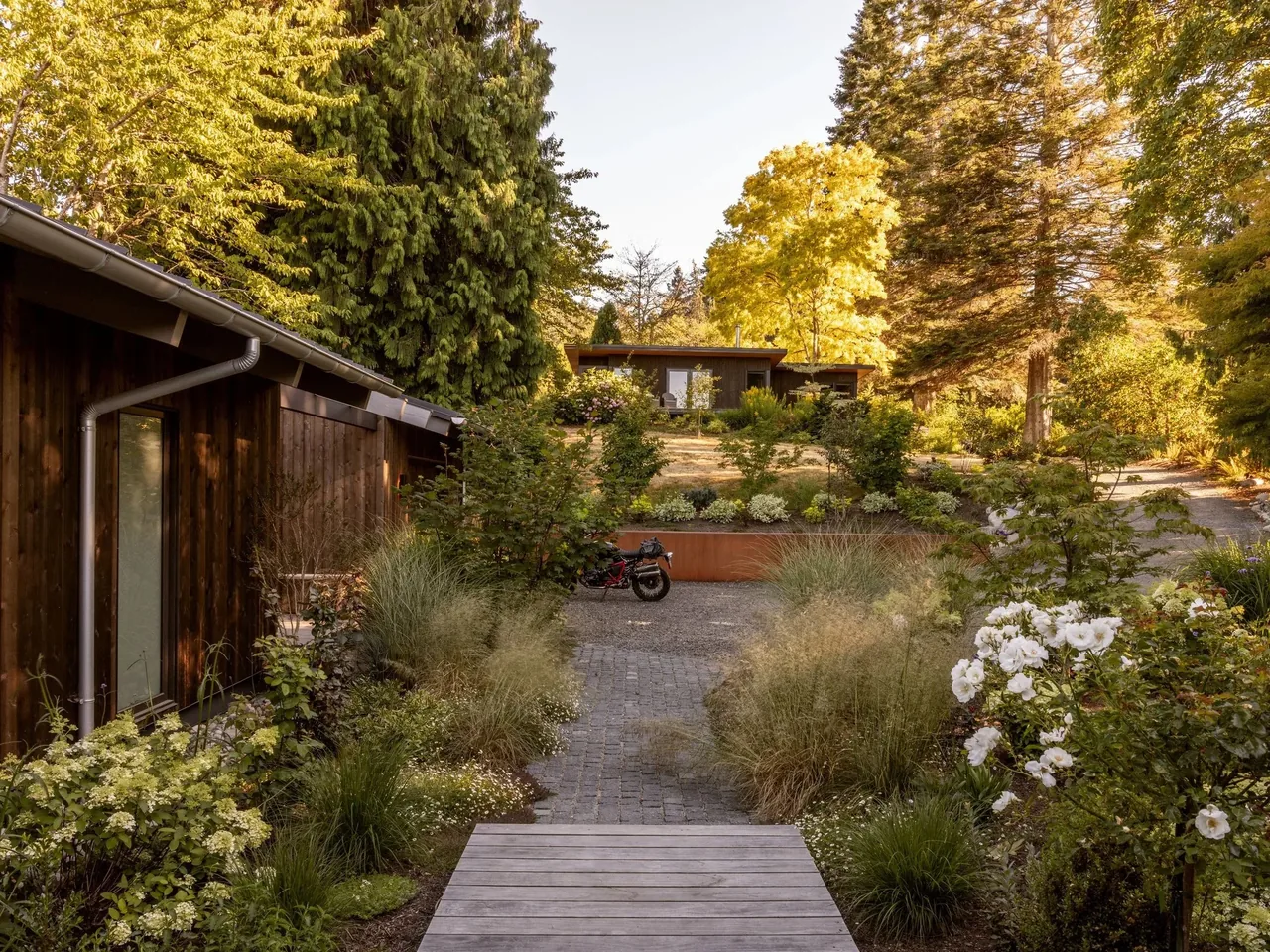 Garden pathway leading to a residence with dark wood siding and large trees around the property.