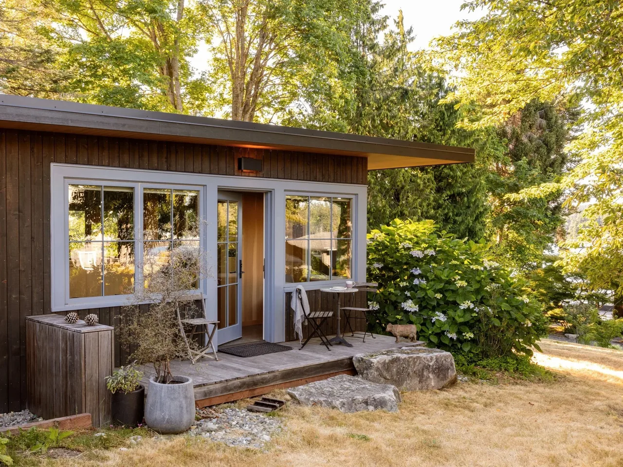 Eagle Harbor Residence features a wood exterior with large windows framed in white and a modest outdoor seating area.