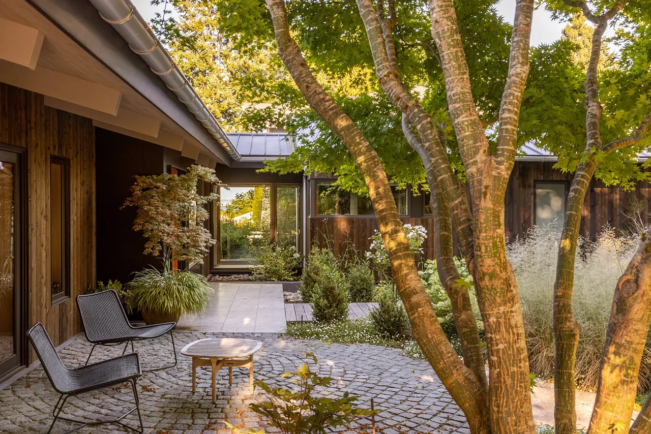 Outdoor courtyard space featuring cobblestone paving and metal seating at the Eagle Harbor Residence by Graham Baba Architects.