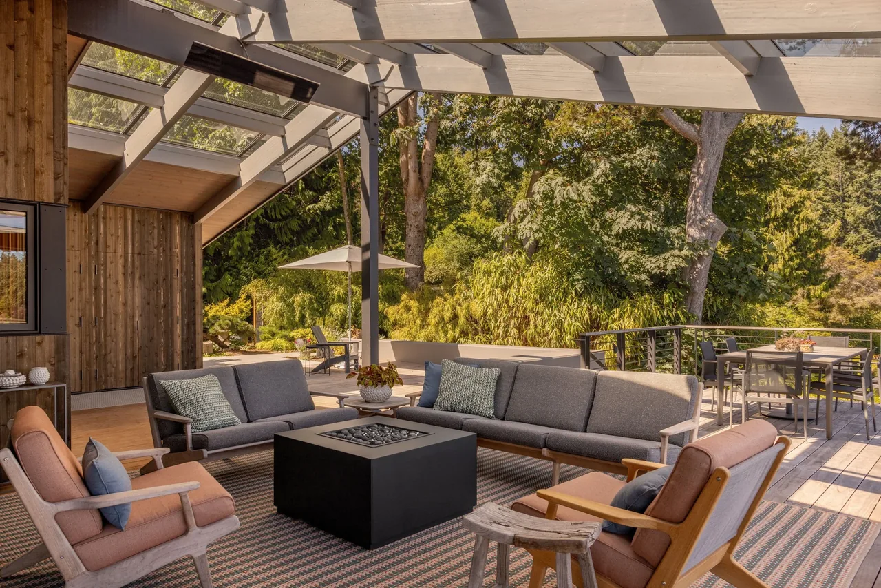 Covered patio with cushioned seating and a fire table at Eagle Harbor Residence by Graham Baba Architects.