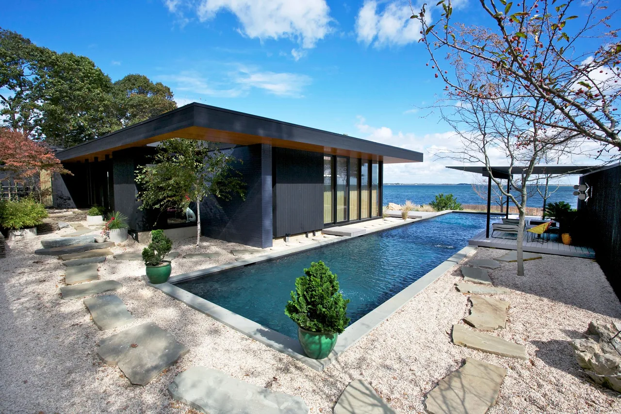 Modern seaside house with a rectangular pool, stepping stone paths, and black wood siding by the water
