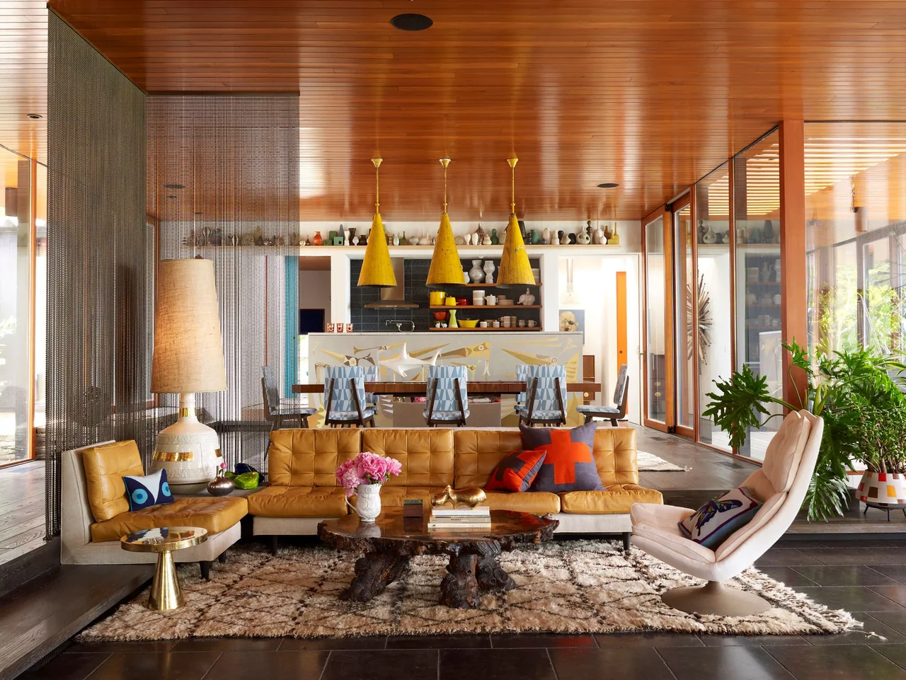 Living and dining rooms feature a caramel leather sofa, yellow pendant lighting, and large windows with wood ceiling.