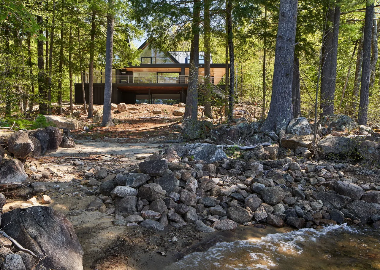 Schroon Lake House by Gray Organschi Architecture nestled in a forested, rocky lakeside setting.