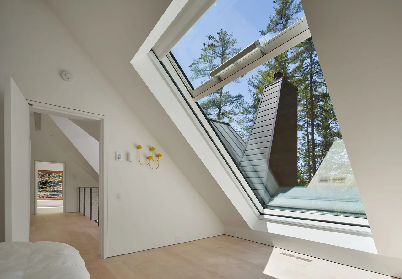 This room features a large triangular window with wood-framed glass panels overlooking a forested area and a chimney.