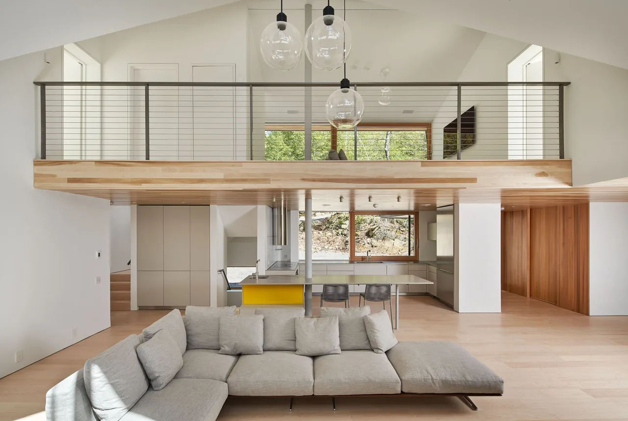 Living room and kitchen of Schroon Lake House featuring a gray sectional sofa and wood-framed window overlooking a rocky landscape.