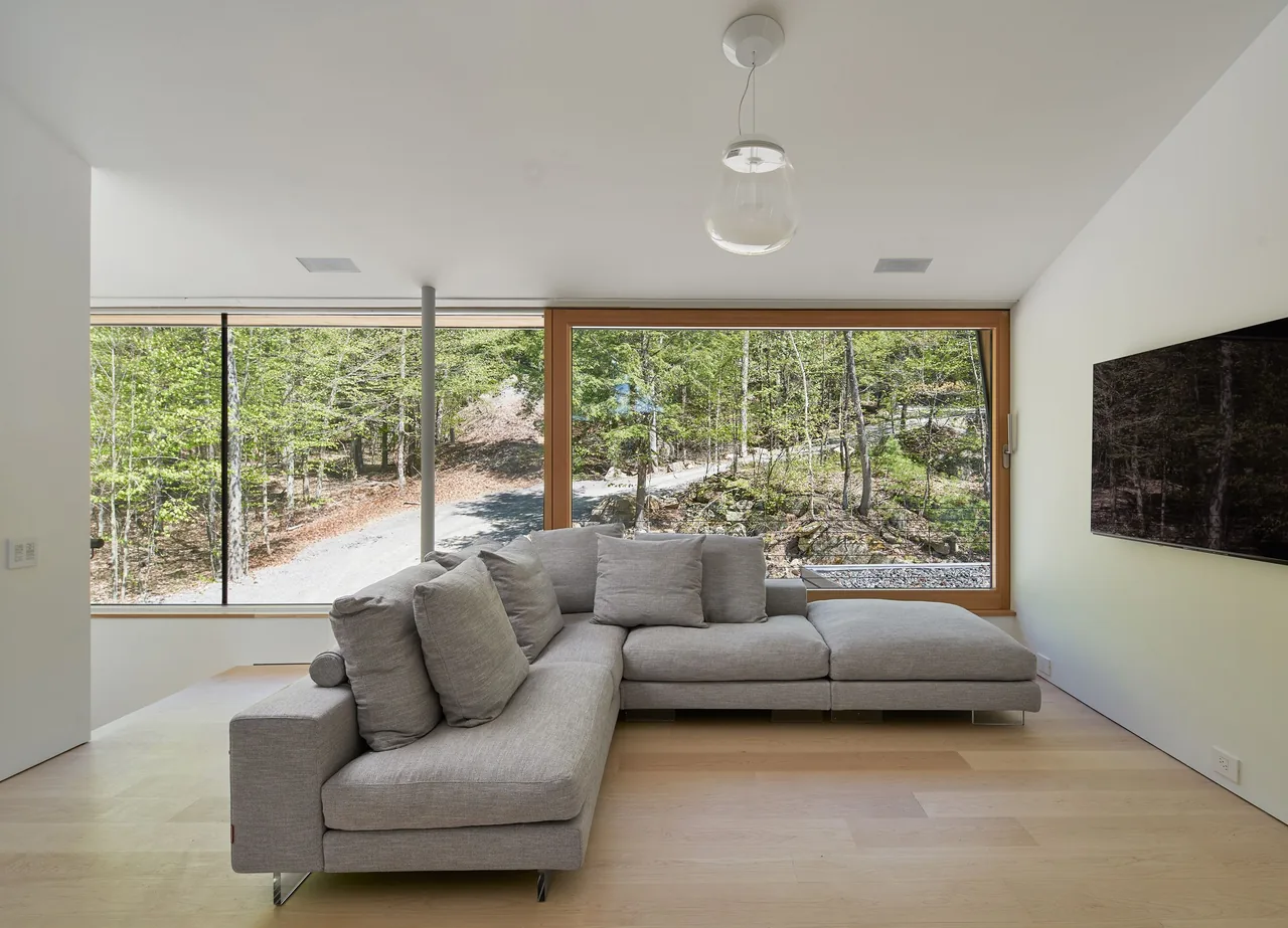 Living room with large picture windows offers extensive views of the wooded surroundings in Schroon Lake House.