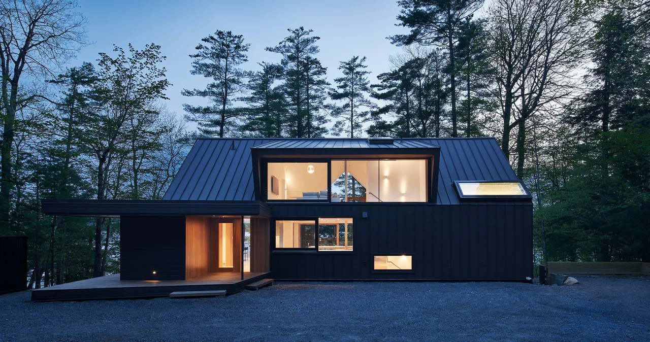 Schroon Lake House features black metal siding, a shed roof, and large wood-framed windows with views of surrounding forest.