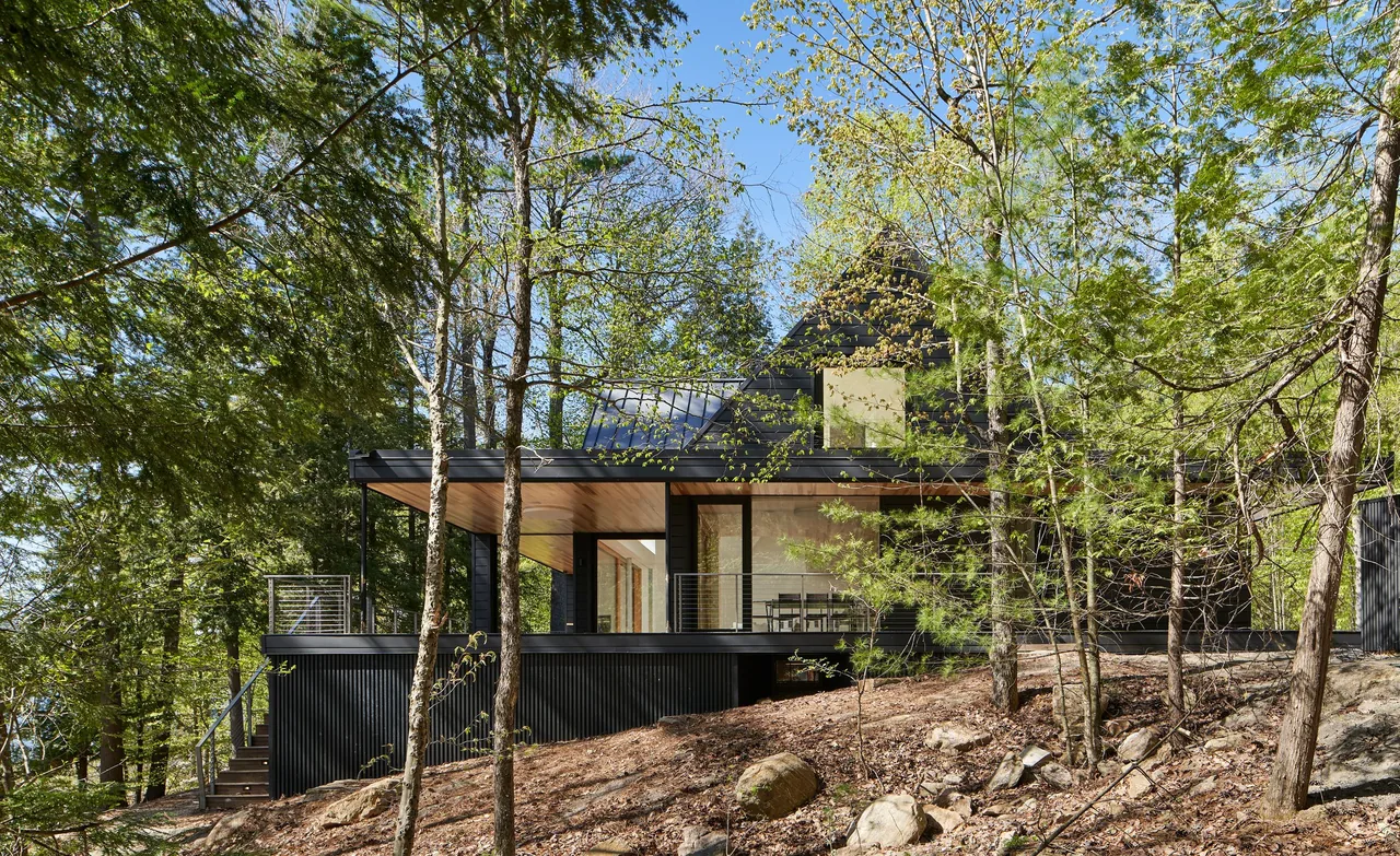 The Schroon Lake House features a black exterior with a covered patio framed by a wooded landscape.