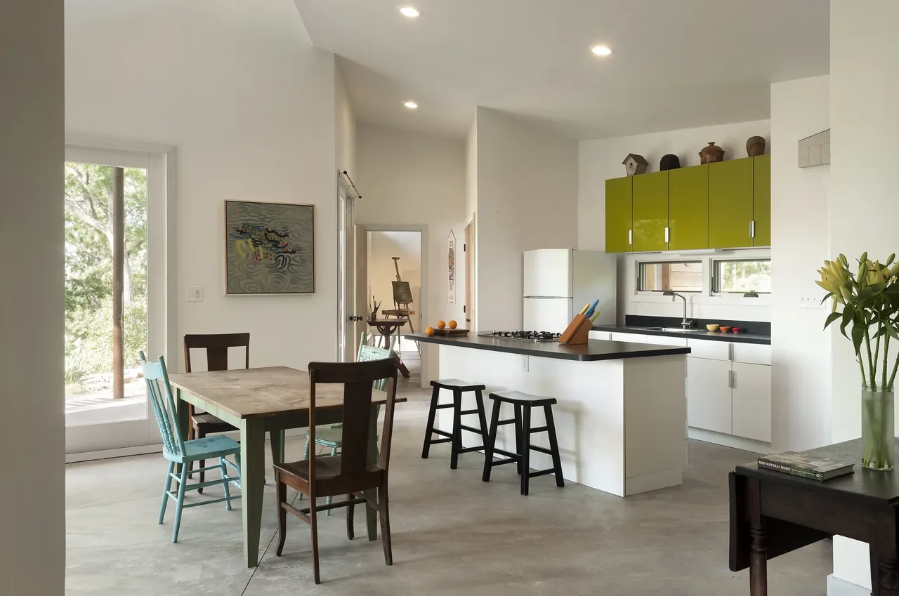 Kitchen and dining space with a kitchen island, green overhead cabinets, and mixed seating around a rustic wooden dining table.