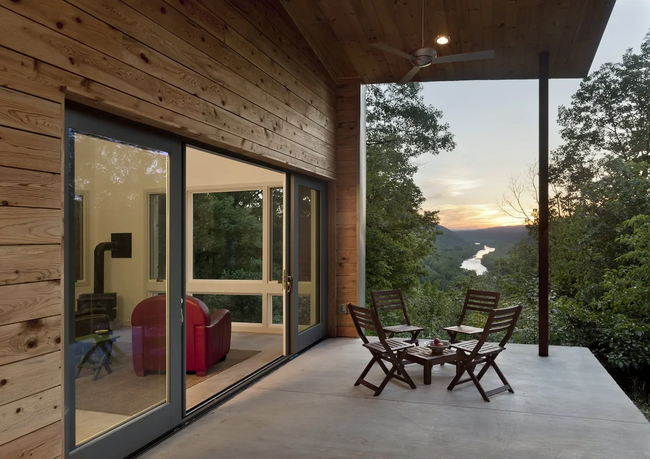 Patio of Ridge House by GriD Architects features wood siding and sliding glass doors with river valley views.