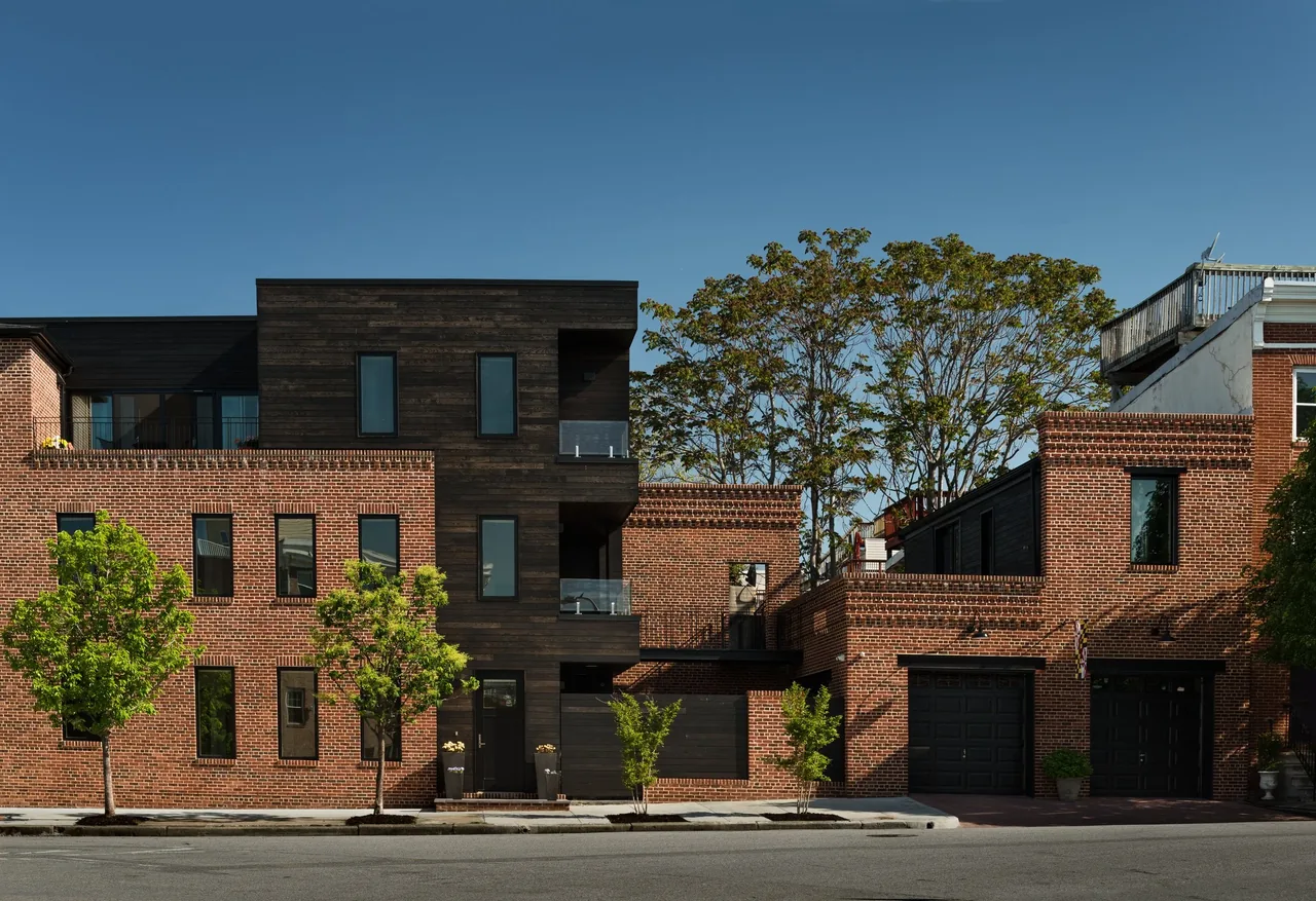 Exterior view of a modern multi-story residential building with brick and dark wood siding under a clear blue sky.