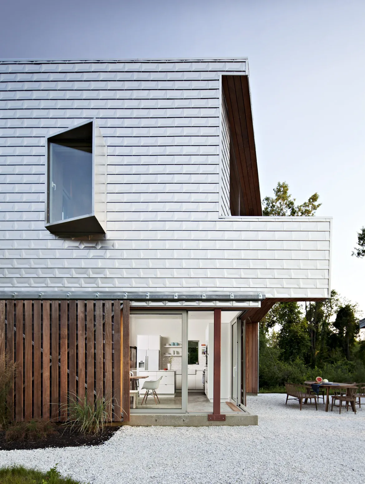 Modern two-story house exterior with white textured siding, large sliding glass door opening to kitchen, and wood slat accent panel.