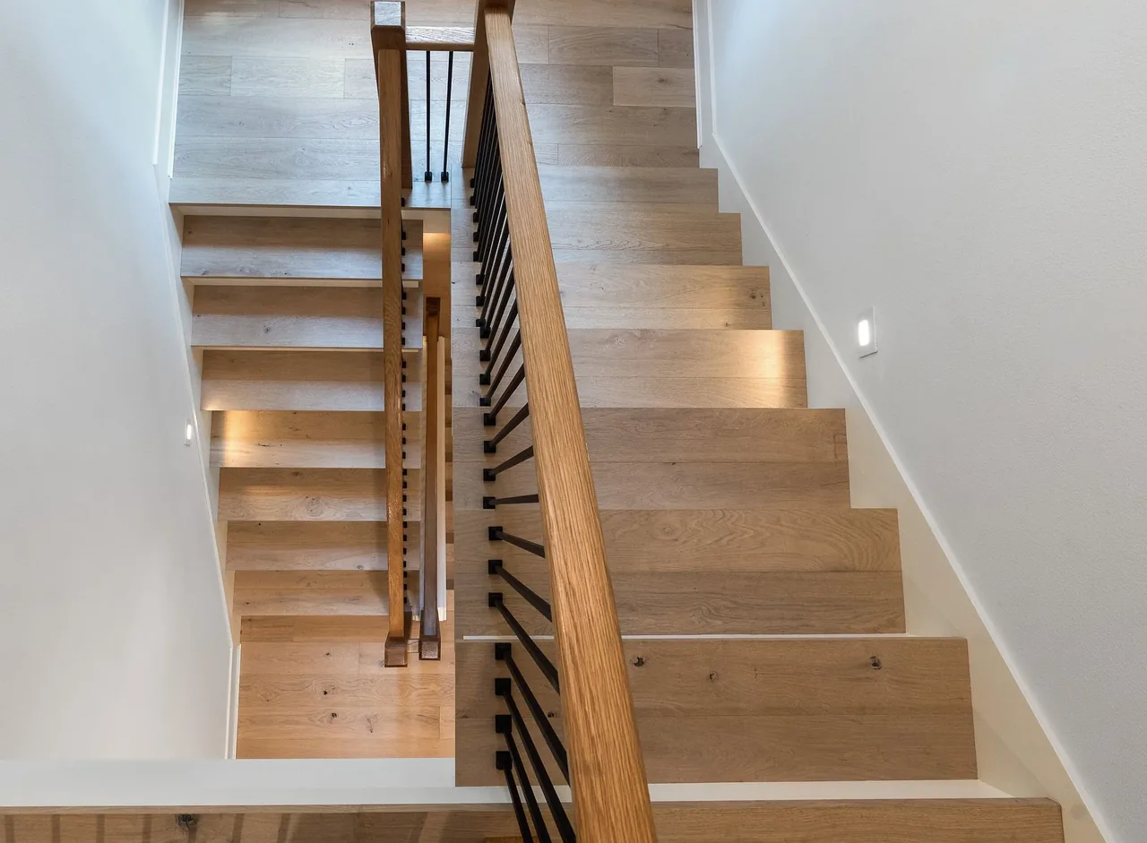 Modern wooden staircase with black metal balusters and integrated wall lighting in a custom home.