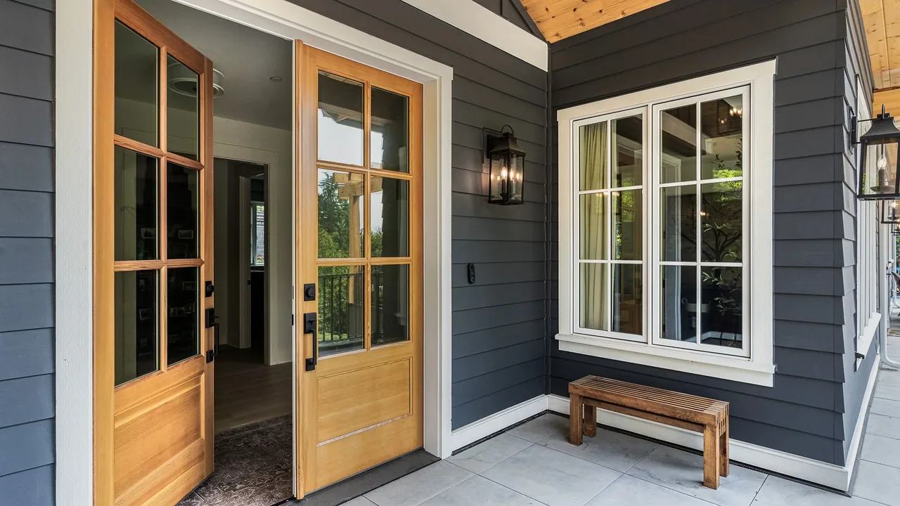 Exterior front porch of Cougar Mt Custom with wood-and-glass doors, gray horizontal siding, and a wooden bench under a window.