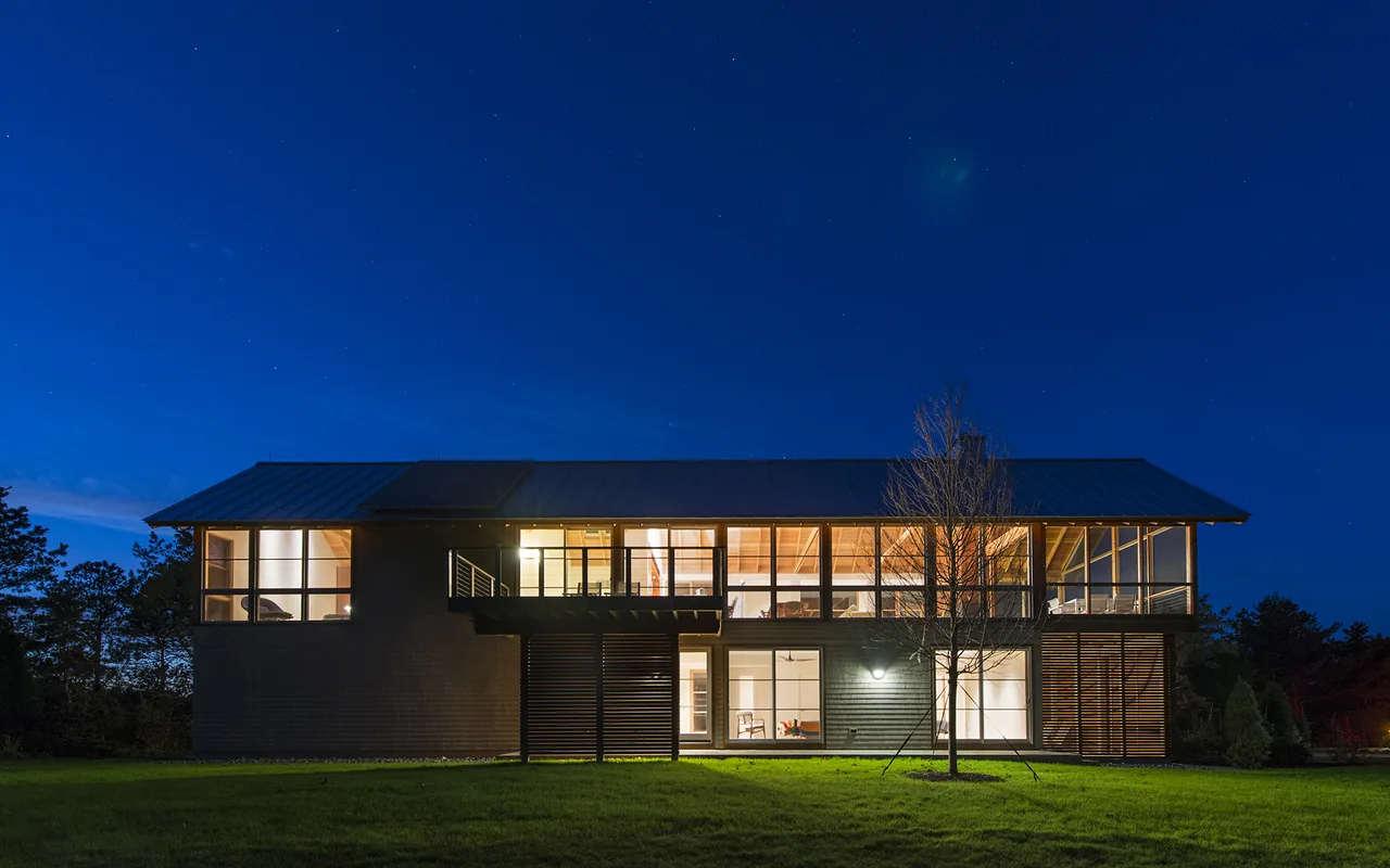 Night exterior of the two-story North Pamet Ridge house with illuminated windows and slatted wood panels on lower level.