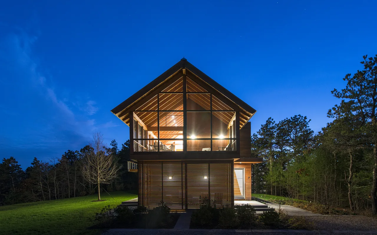 The North Pamet Ridge House features a two-story design with floor-to-ceiling glazing and slatted wood panels under a gable roof.