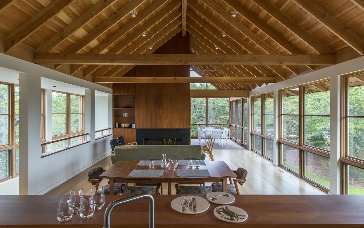 Interior of North Pamet Ridge House featuring vaulted wood ceiling, floor-to-ceiling glazing, and a central fireplace wall.