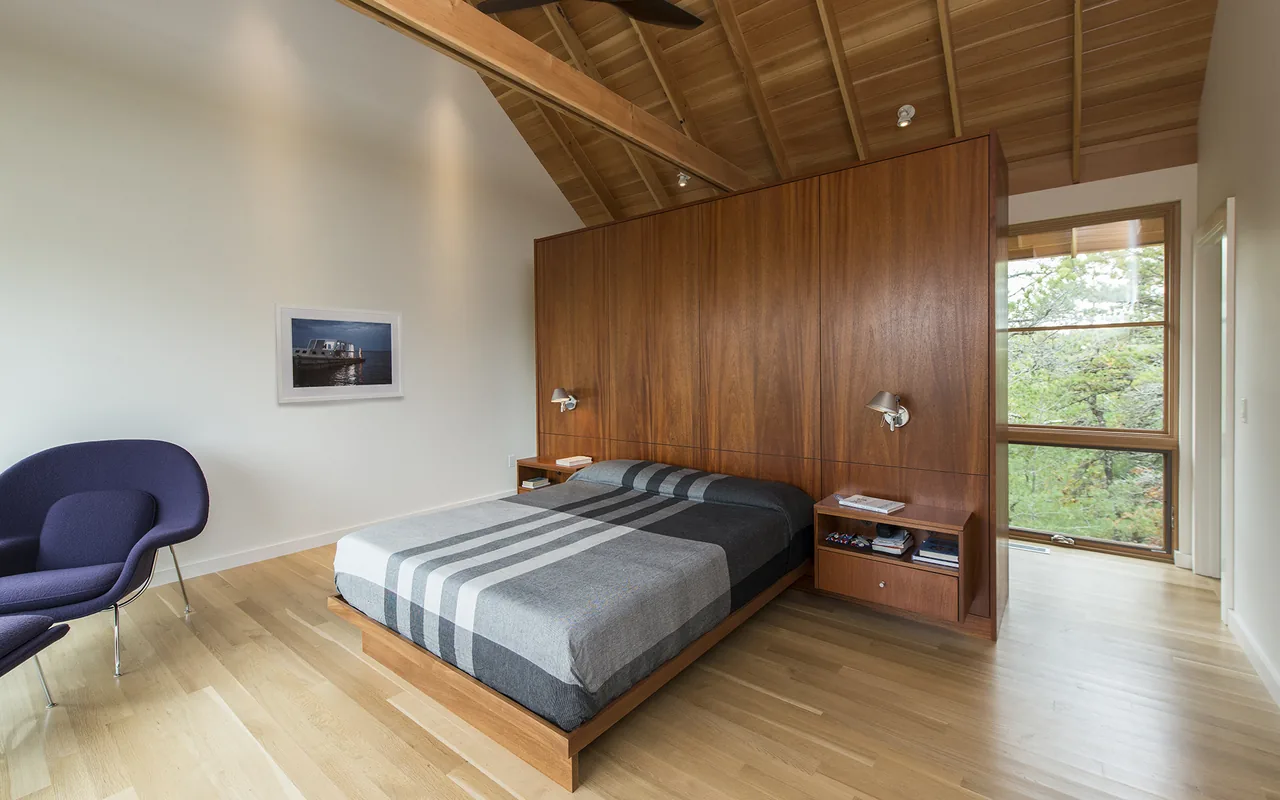 Bedroom with wooden platform bed, built-in nightstands with sconces, and large windows providing natural light.