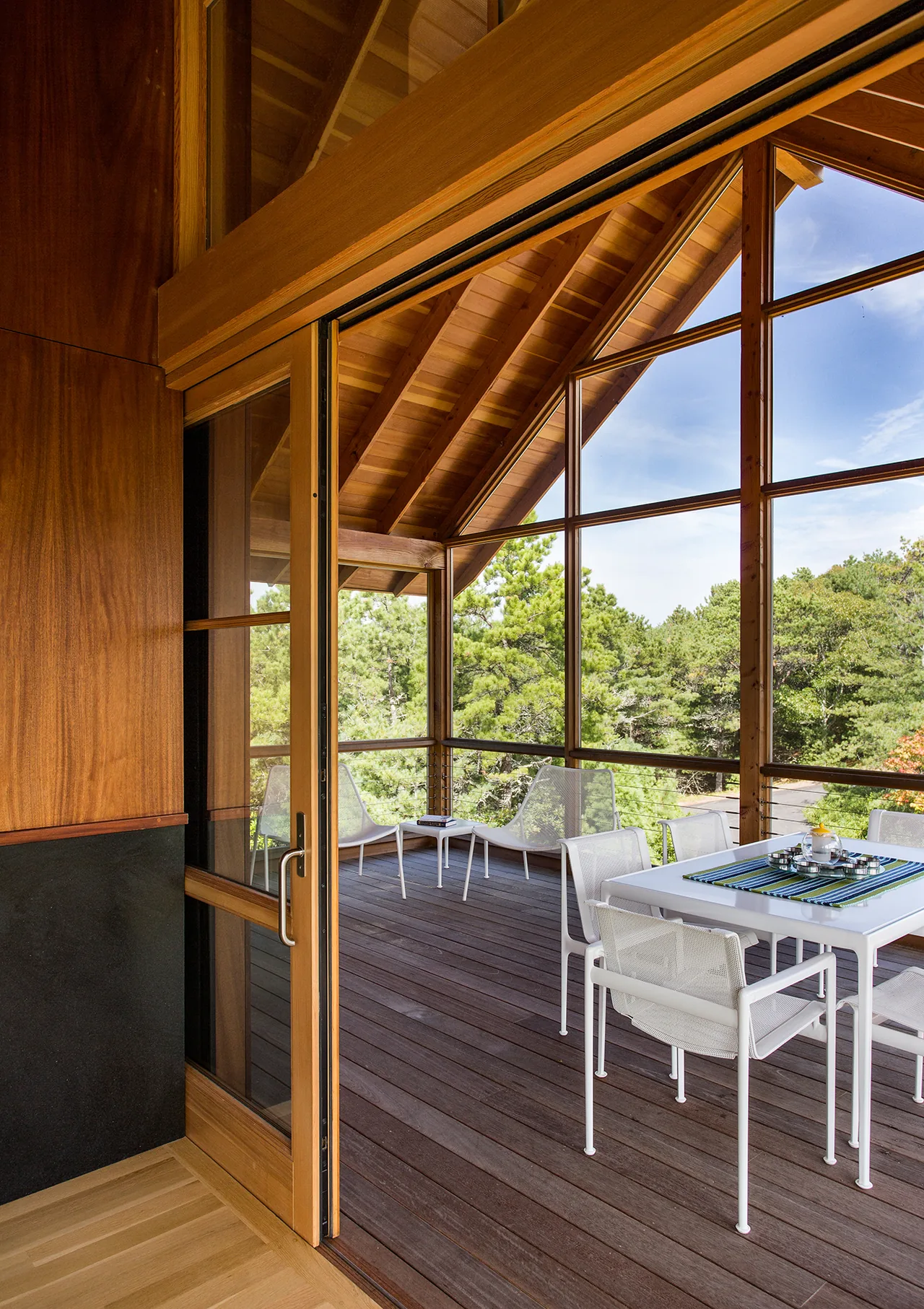 Screened porch with vaulted wooden ceiling and seating, overlooking green trees.
