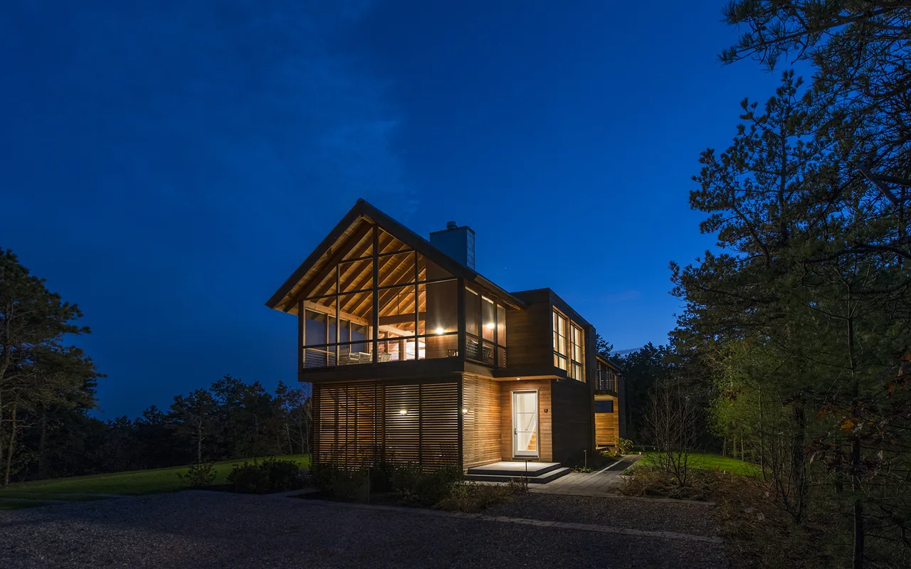 North Pamet Ridge House in Truro by Hammer Architects features mixed wood siding, large windows, and a raised covered porch at night.