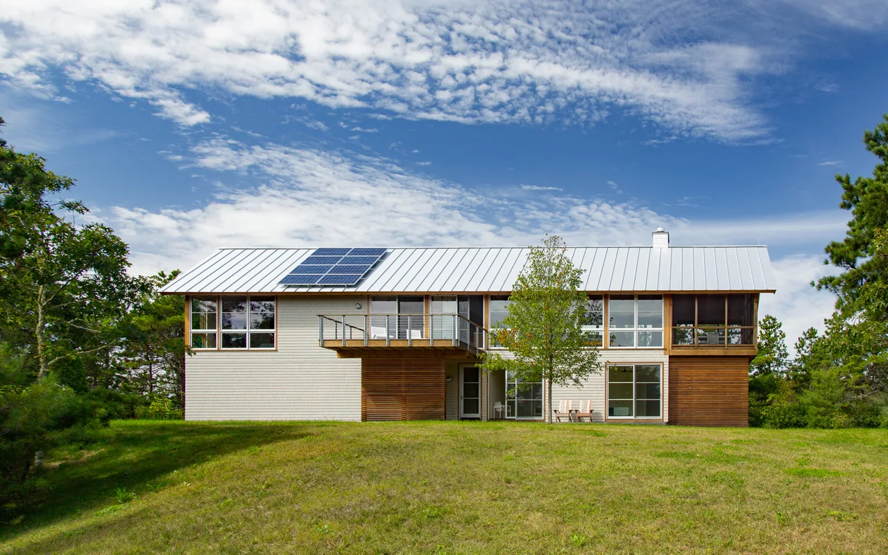 Rear exterior of North Pamet Ridge House by Hammer Architects featuring mixed wood siding and a metal roof with solar panels.