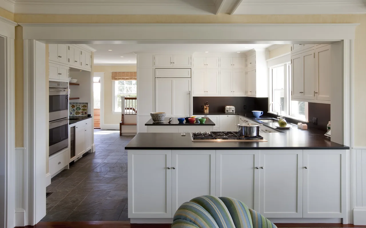 The Watch Hill Rhode Island Residence kitchen features white cabinetry, black countertops, and a central island with a gas range cooktop.