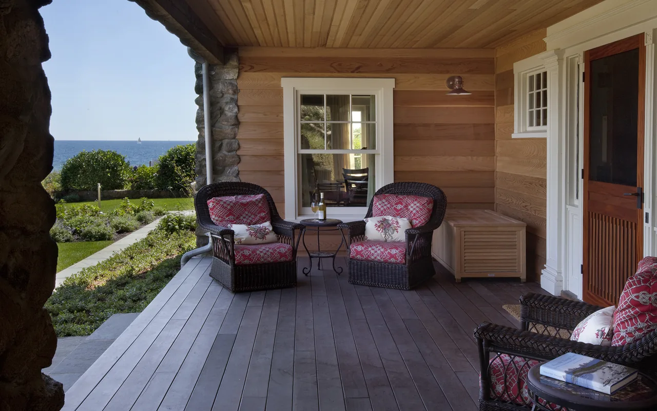 Covered porch with wicker seating and ocean view at Watch Hill Rhode Island Residence by Hammer Architects.