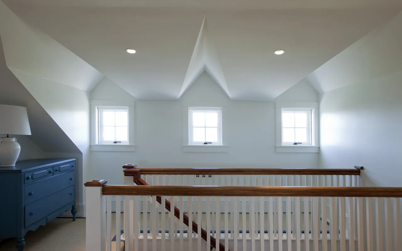 Hallway with three small windows and wooden railing overlooking staircase in a residential home.