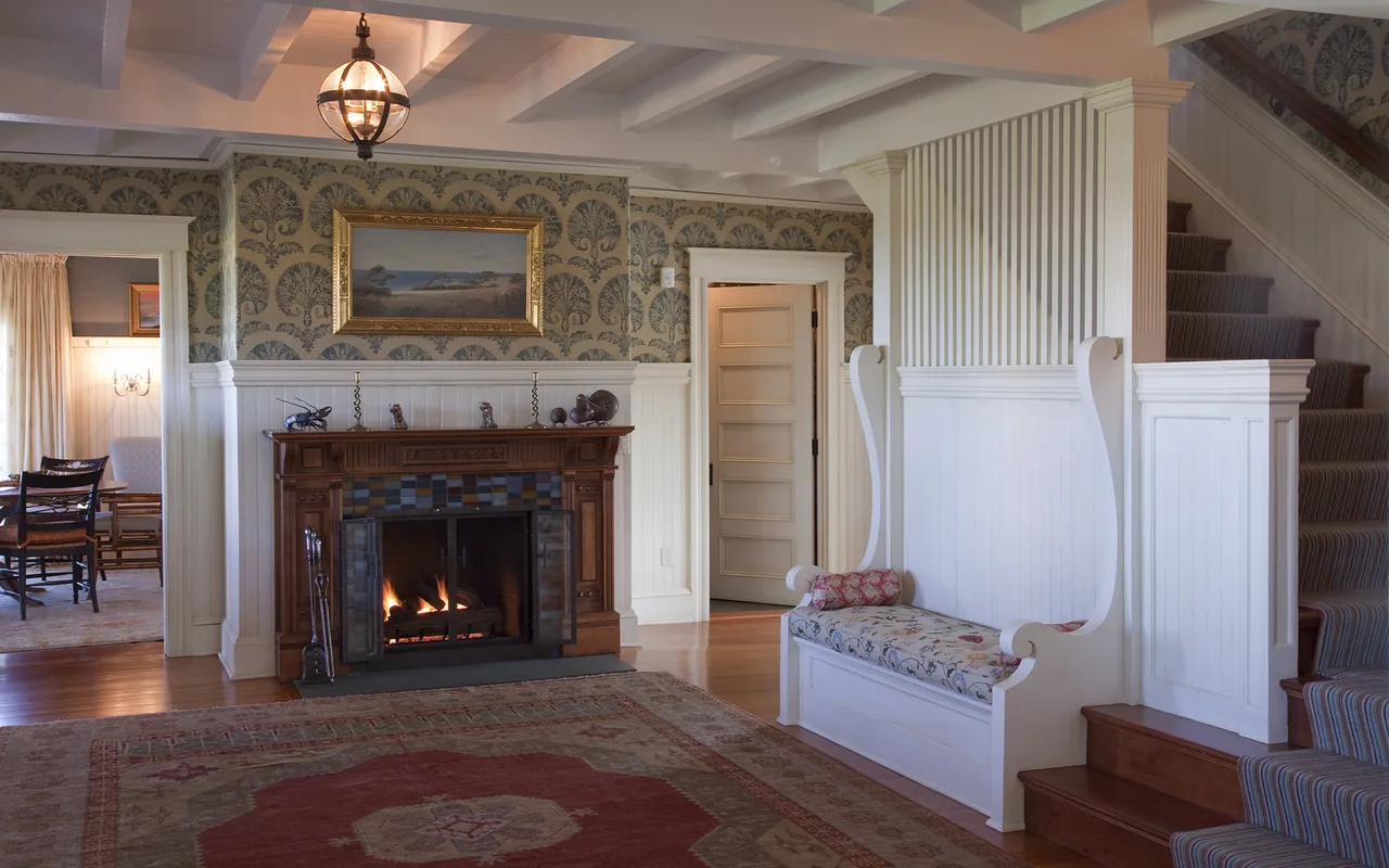 Living room featuring a lit fireplace with a wooden mantel and a floral wallpaper above wainscoting.