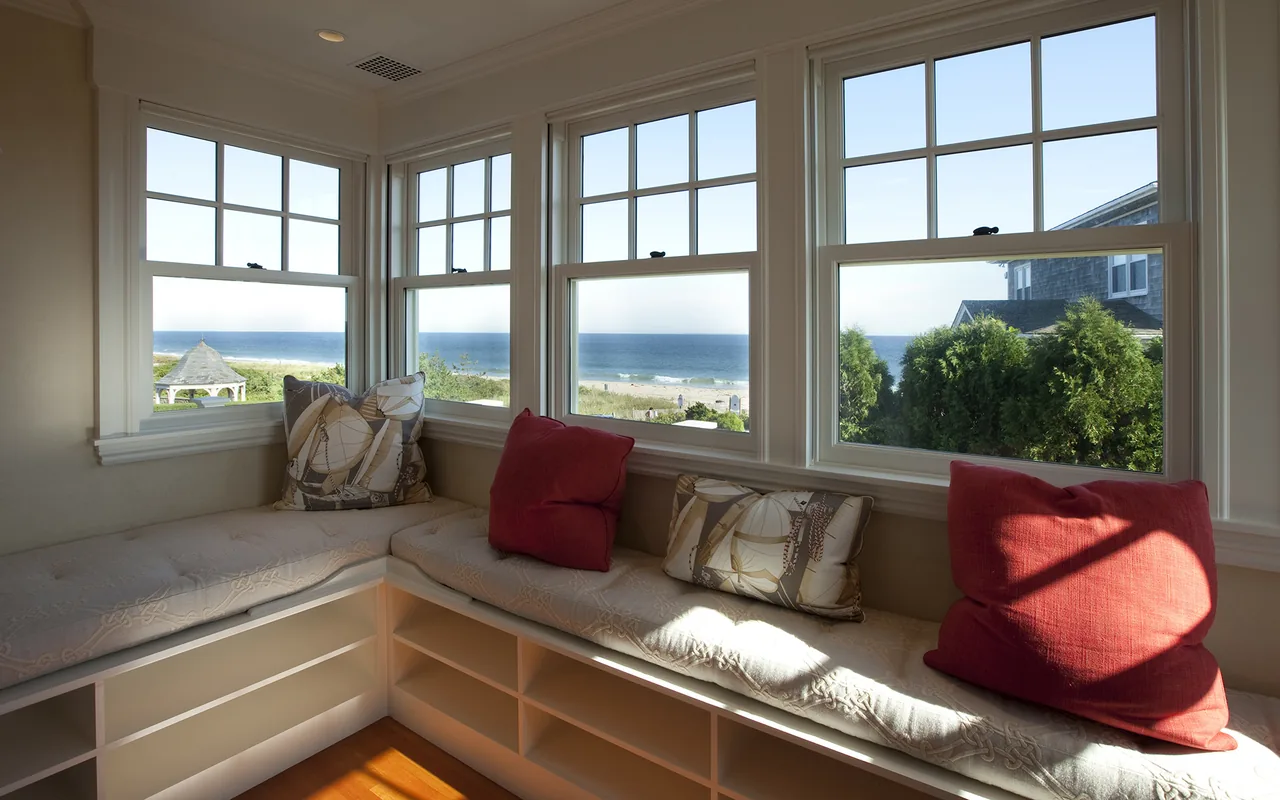 Built-in bench with cushions along corner windows framing ocean views in a sunlit room.