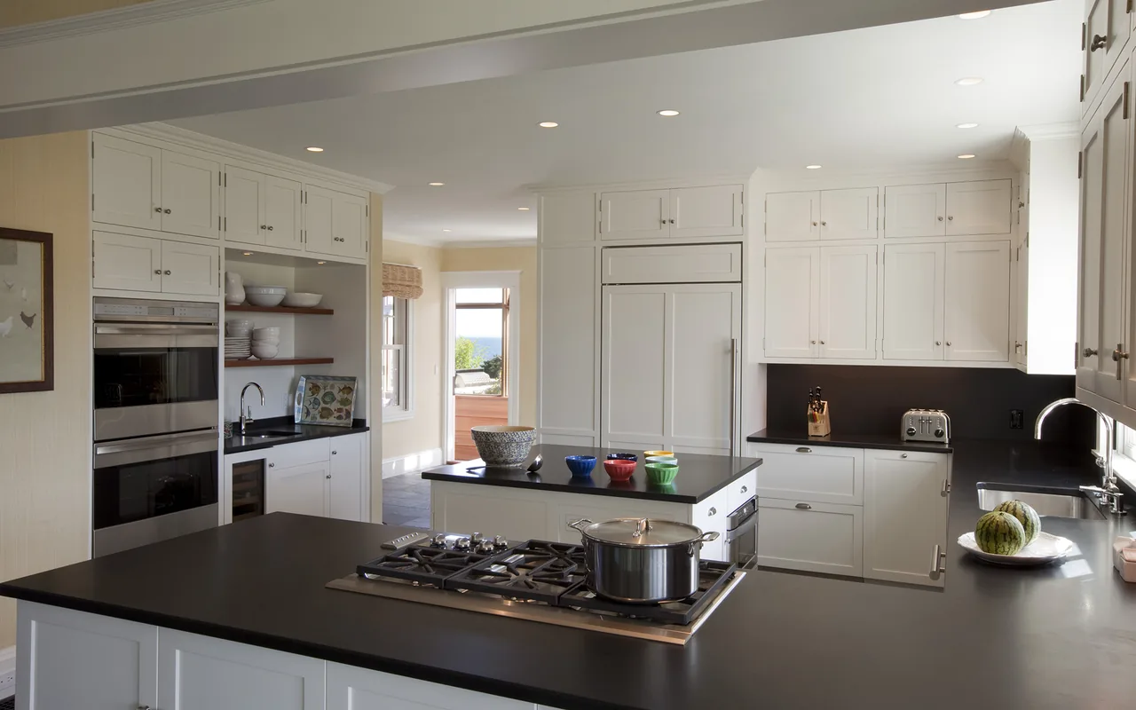 Kitchen in Watch Hill Rhode Island Residence features white cabinetry, black countertops, a gas range, and built-in ovens.