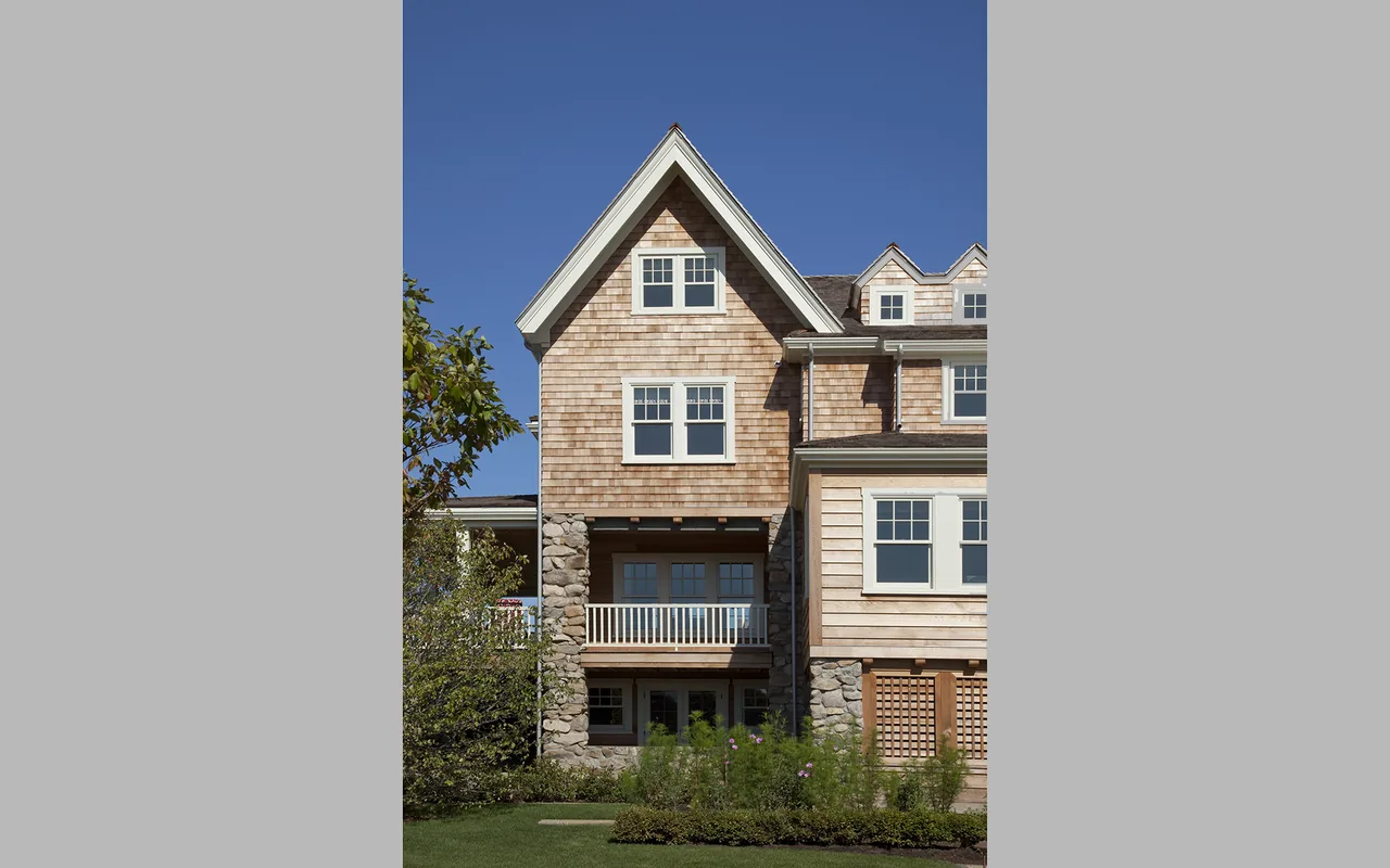 The Watch Hill Rhode Island Residence features wood shingle siding with stone accents under a clear blue sky.