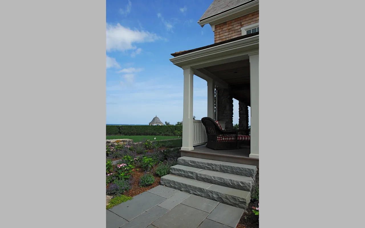 Porch with stone foundation steps and wicker seating at Watch Hill Rhode Island Residence by Hammer Architects.
