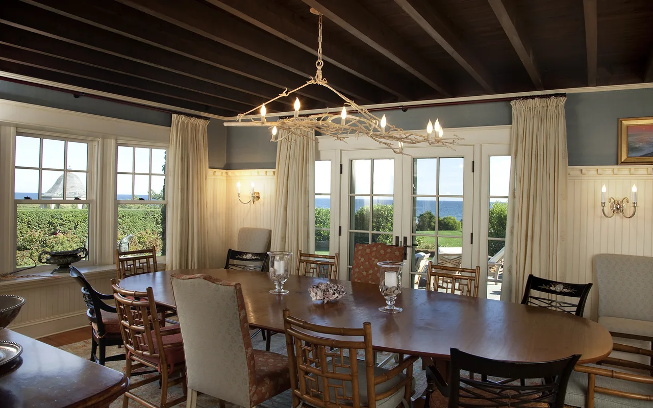 Dining room with wood ceiling beams and glass doors offering ocean views at the Watch Hill Rhode Island Residence.