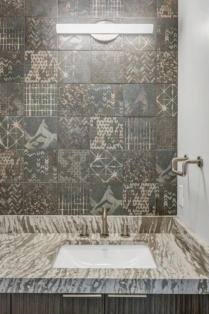 Bathroom vanity features an undermount sink, textured dark patterned tile backsplash, and a marbled countertop.