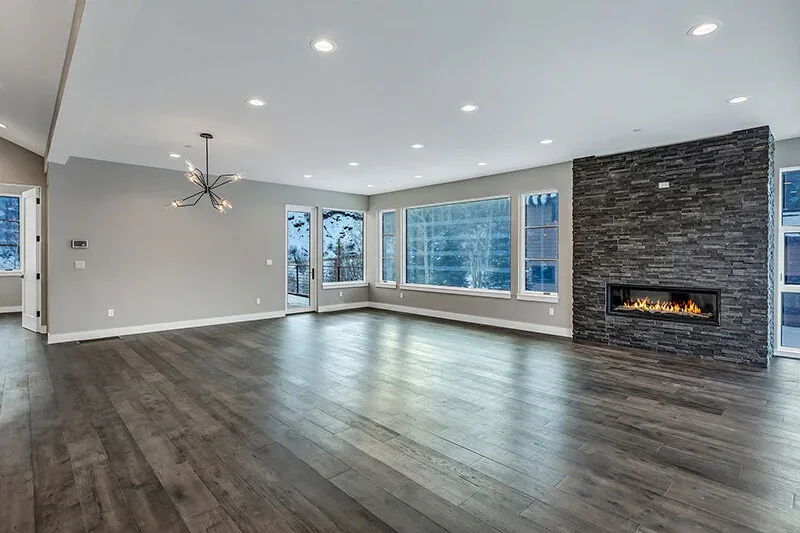 Living room featuring rough cut stone fireplace, horizontal wood plank floors, and large windows with mountain views and snowy landscape.