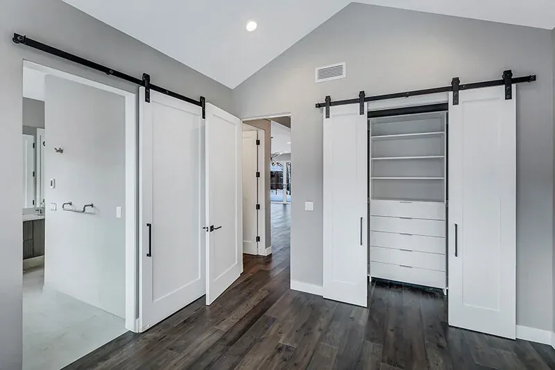 Interior room with vaulted ceiling, white sliding barn doors, and adjacent bathroom entry.