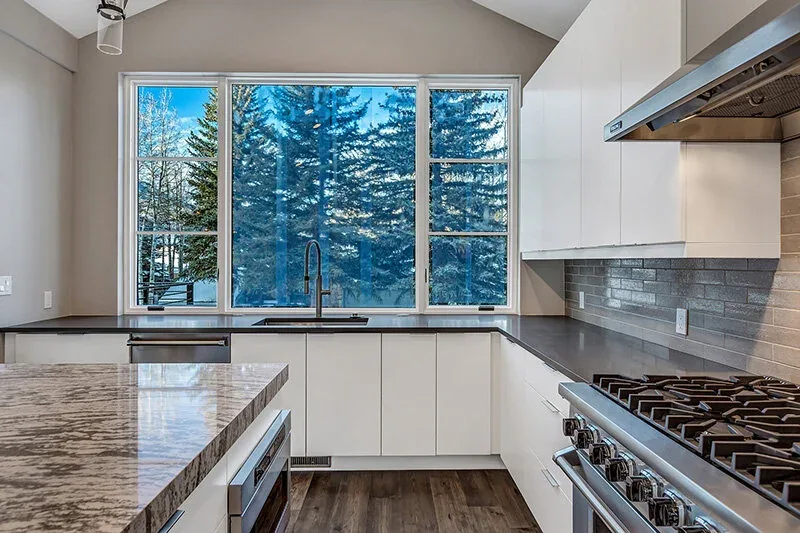 Kitchen with white cabinets, marble island, black countertops, and large windows overlooking snowy trees.