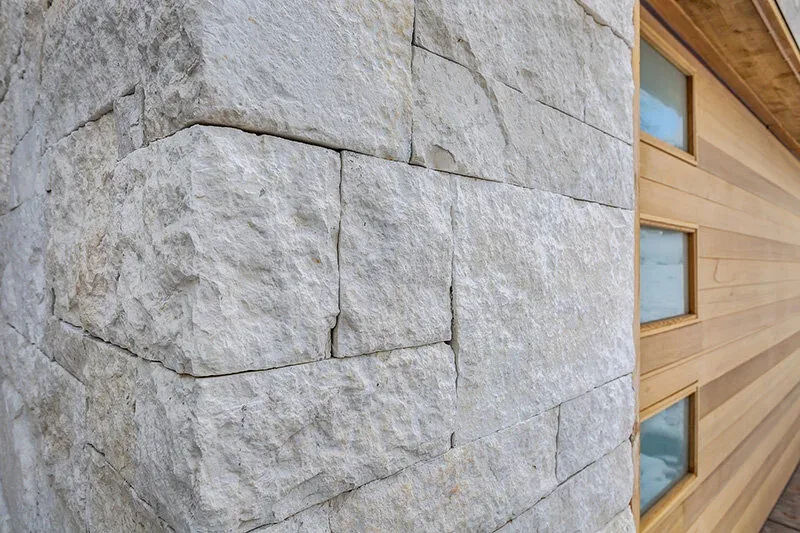 Exterior corner showing rough limestone blocks and adjacent wood siding with four rectangular windows.