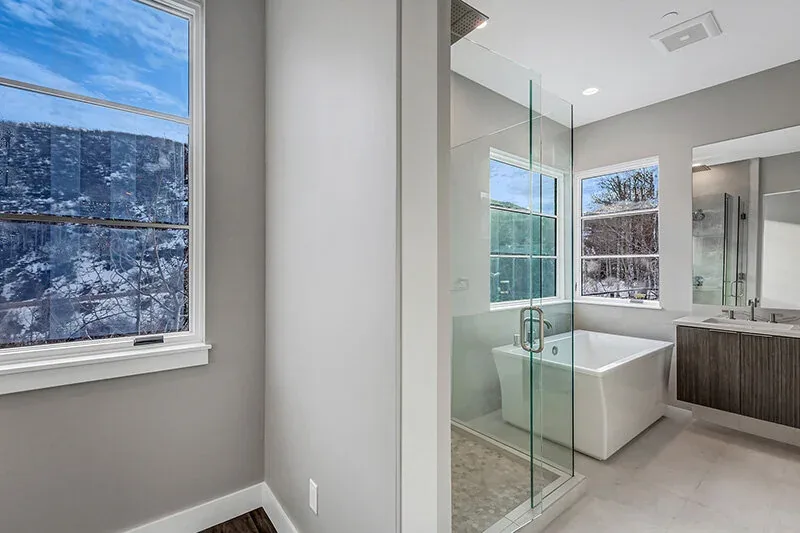 Bathroom featuring a freestanding tub, glass shower, and dual sinks with large windows overlooking a snowy view.