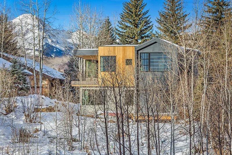 The Snowmass Village Weekender house features mixed wood and gray siding with large windows and a gable roof.